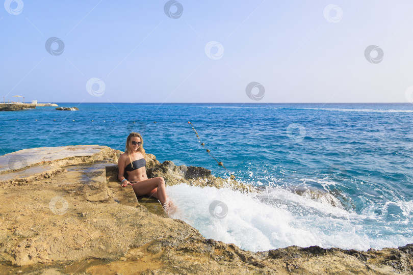 Скачать Молодая девушка в купальнике сидит на ступеньках утеса на берегу моря. фотосток Ozero