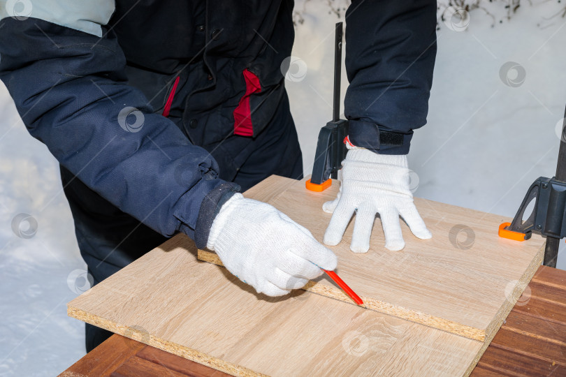 Скачать Мужчина, рабочий рисует карандашом на доске из ДСП. фотосток Ozero