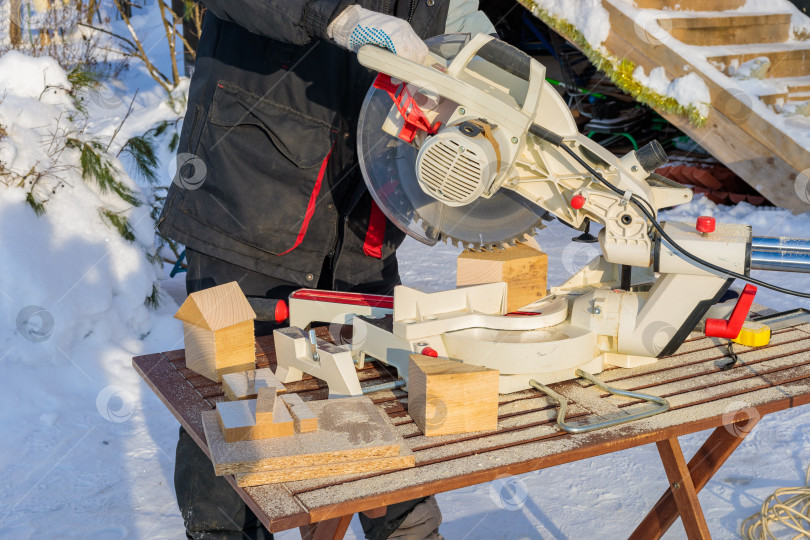 Скачать Рабочий-мужчина распиливает брусок электрической пилой с диском. фотосток Ozero