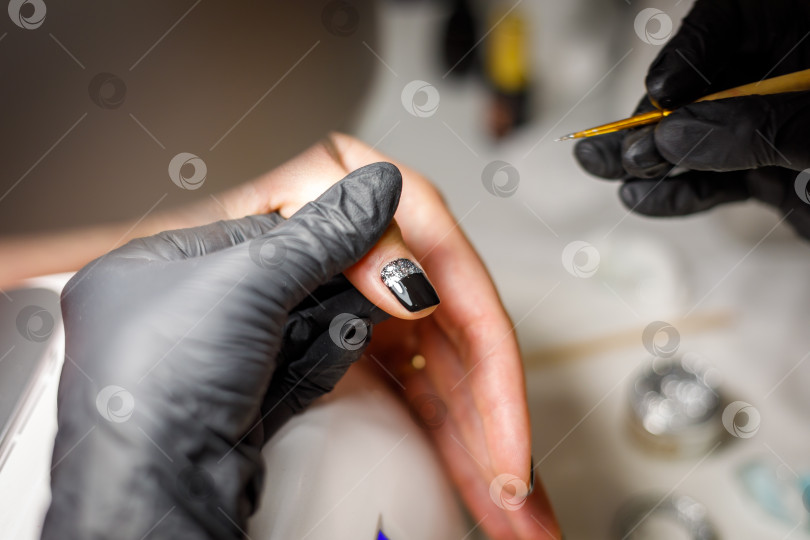 Скачать В студии красоты мастер делает маникюр, наносит кисточкой рисунок на ноготь. фотосток Ozero