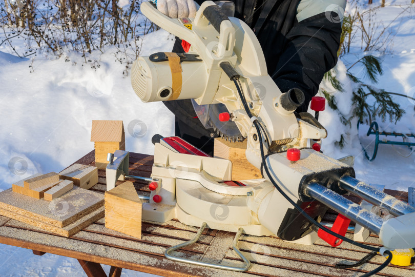 Скачать Рабочий-мужчина распиливает брусок электрической пилой с диском. фотосток Ozero