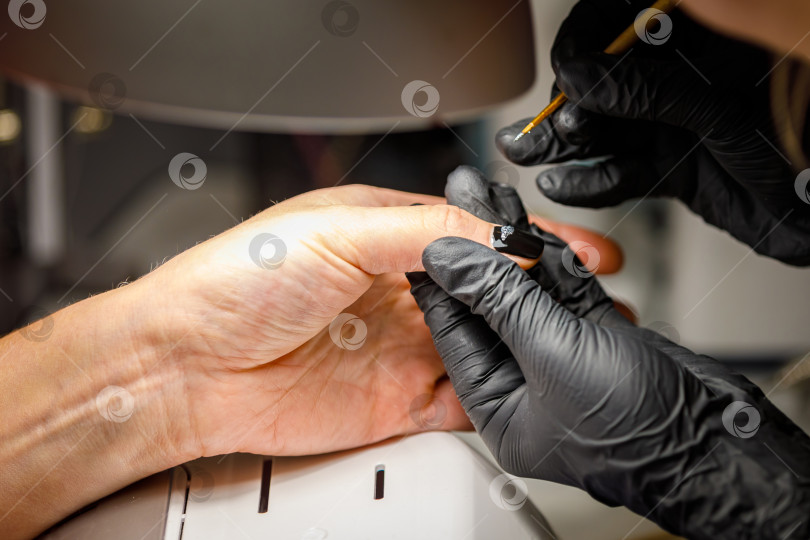 Скачать В студии красоты мастер делает маникюр, наносит кисточкой рисунок на ноготь. фотосток Ozero