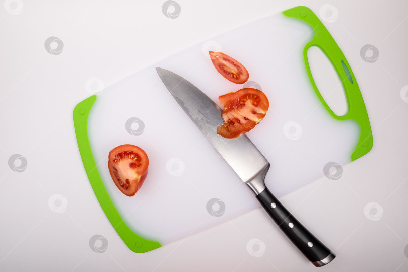 Скачать На разделочной доске лежит нарезанный свежий красный помидор и большой поварской нож. фотосток Ozero