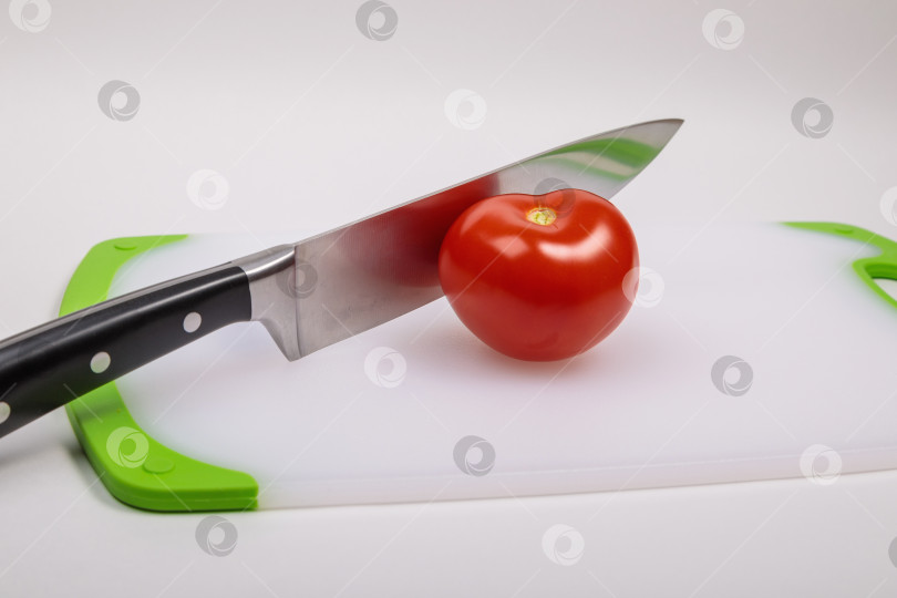 Скачать На разделочной доске лежат свежий красный помидор и большой поварской нож. фотосток Ozero