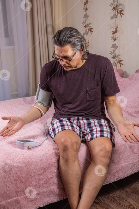 Скачать 50-летний мужчина измеряет свое кровяное давление с помощью тонометра. фотосток Ozero