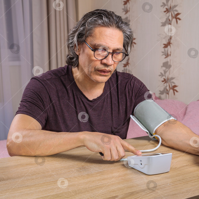 Скачать 50-летний мужчина измеряет свое кровяное давление с помощью тонометра. фотосток Ozero