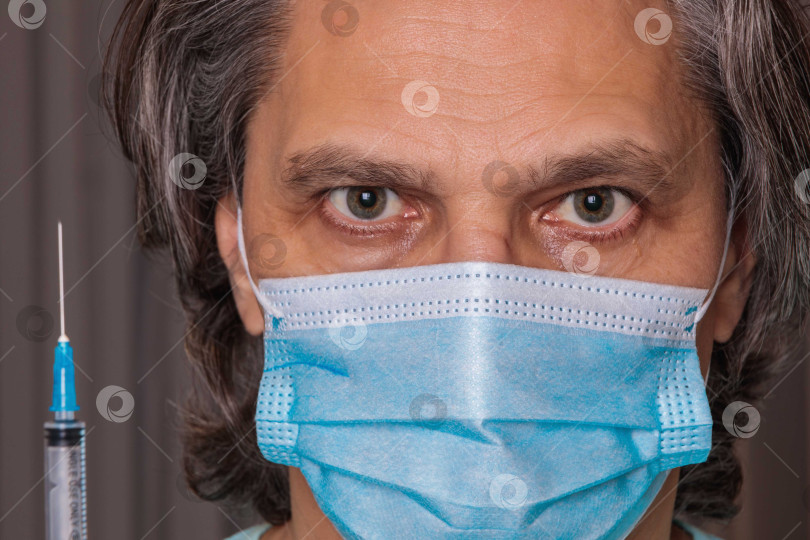 Скачать Взрослый мужчина в медицинской маске. Глаза крупным планом. Шприц в руке фотосток Ozero