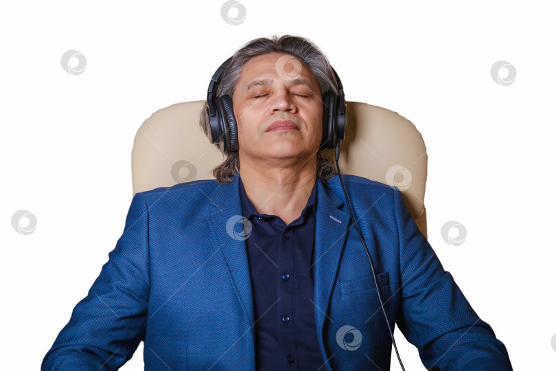 Скачать 50-летний мужчина слушает музыку в наушниках дома, сидя в кресле. фотосток Ozero