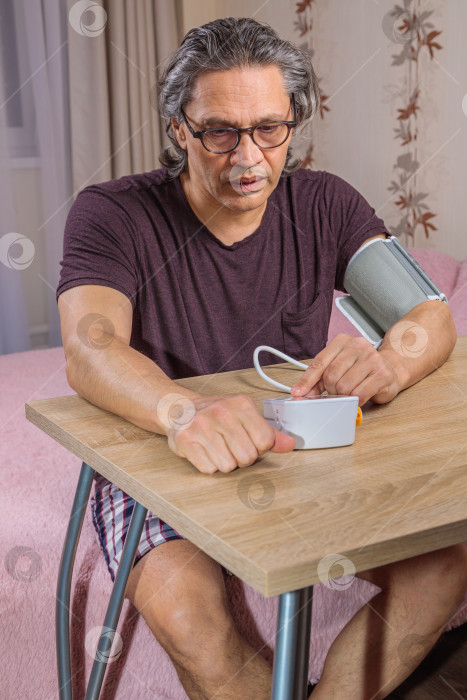 Скачать 50-летний мужчина измеряет свое кровяное давление с помощью тонометра. фотосток Ozero