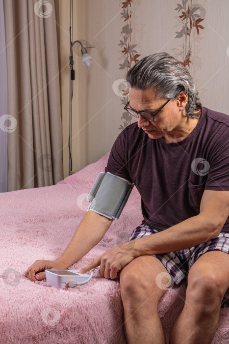 Скачать 50-летний мужчина измеряет свое кровяное давление с помощью тонометра. фотосток Ozero