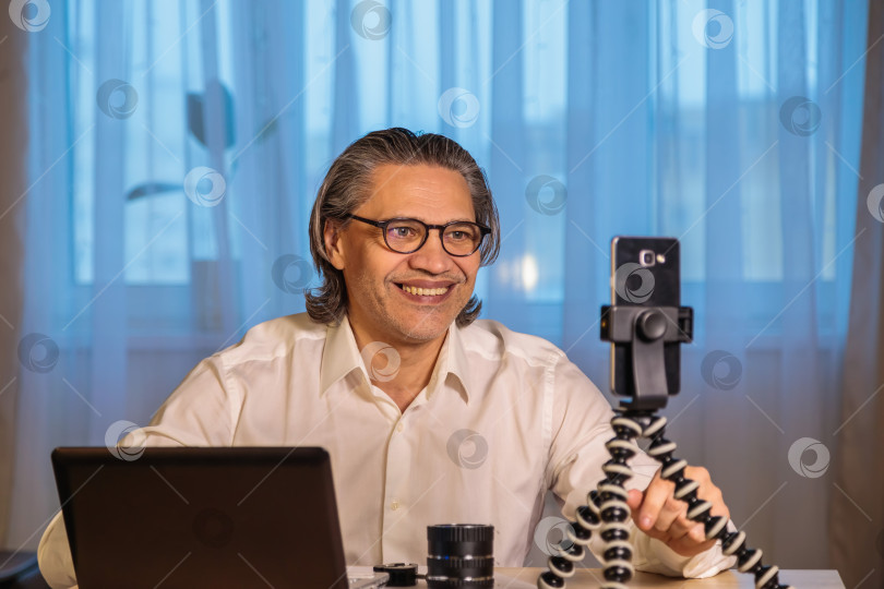 Скачать 50-летний блогер в очках записывает видео из дома на свой смартфон. фотосток Ozero