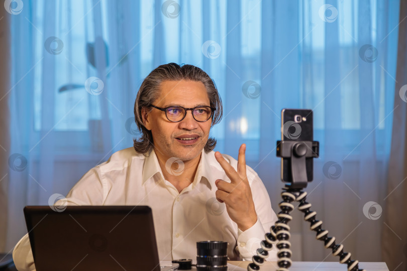 Скачать 50-летний блогер в очках записывает видео из дома на свой смартфон. фотосток Ozero