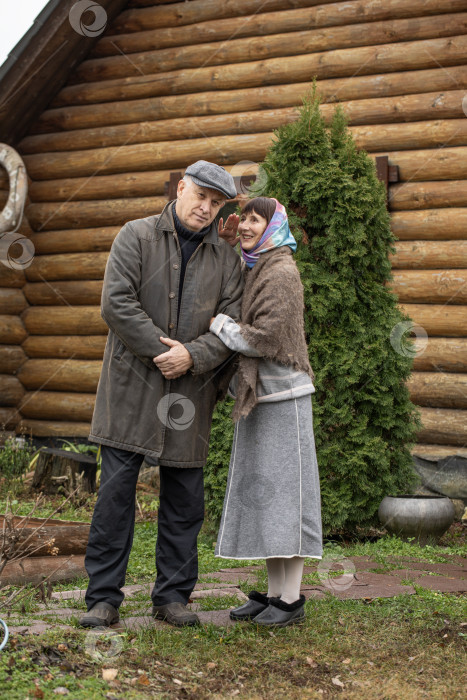 Скачать Деревенская пара пенсионеров позирует возле бревенчатой бани. фотосток Ozero