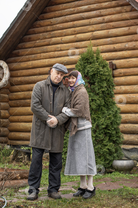 Скачать Деревенская пара пенсионеров позирует возле бревенчатой бани. фотосток Ozero