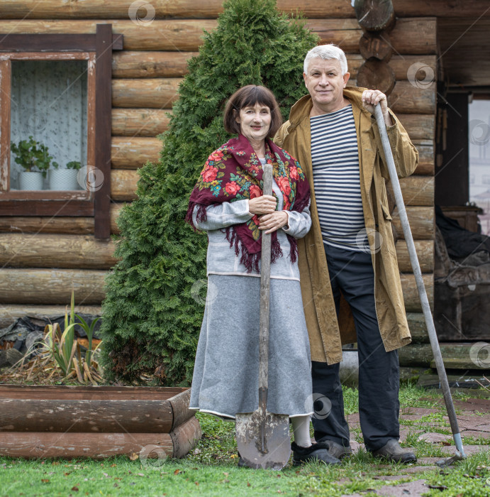 Скачать Деревенская пара пенсионеров позирует возле бревенчатой бани. фотосток Ozero