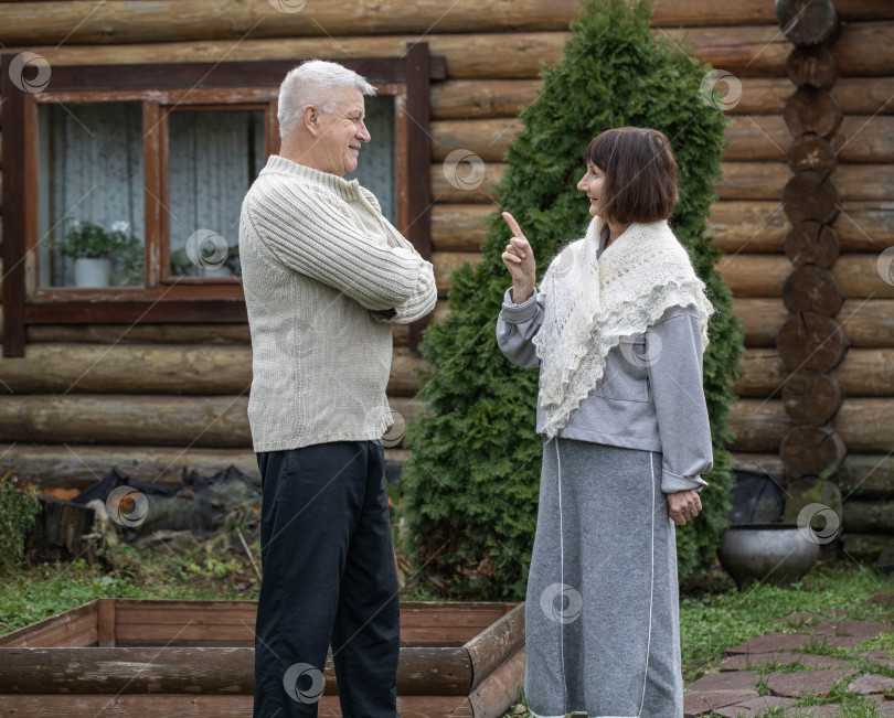 Скачать Деревенская пара пенсионеров позирует возле бревенчатой бани. фотосток Ozero