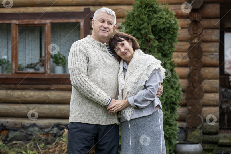 Скачать Деревенская пара пенсионеров позирует возле бревенчатой бани. фотосток Ozero