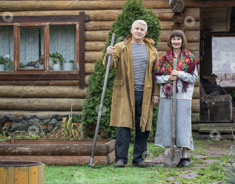Скачать Деревенская пара пенсионеров позирует возле бревенчатой бани. фотосток Ozero