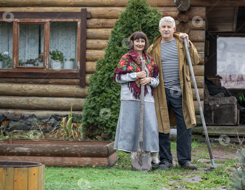 Скачать Деревенская пара пенсионеров позирует возле бревенчатой бани. фотосток Ozero