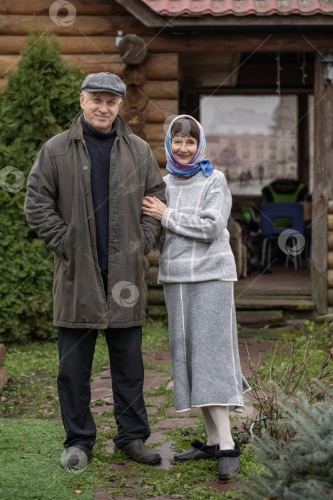Скачать Деревенская пара пенсионеров позирует возле бревенчатой бани. фотосток Ozero