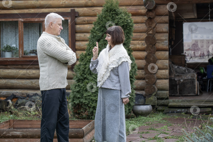 Скачать Деревенская пара пенсионеров позирует возле бревенчатой бани. фотосток Ozero