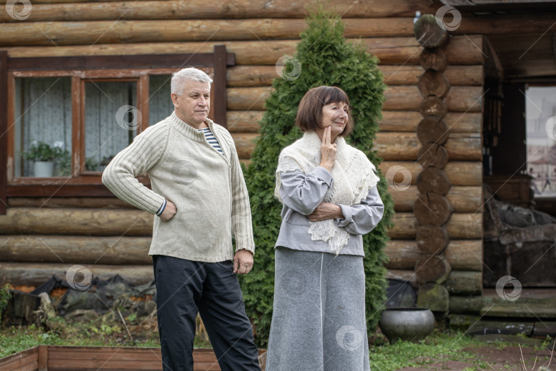 Скачать Деревенская пара пенсионеров позирует возле бревенчатой бани. фотосток Ozero