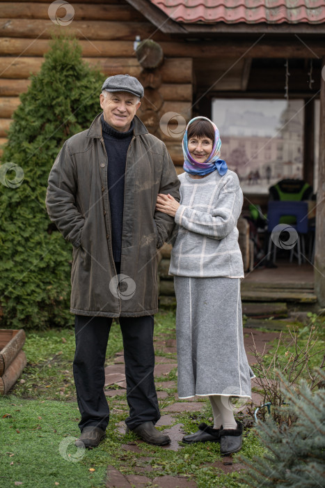 Скачать Деревенская пара пенсионеров позирует возле бревенчатой бани. фотосток Ozero