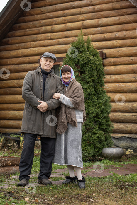 Скачать Деревенская пара пенсионеров позирует возле бревенчатой бани. фотосток Ozero