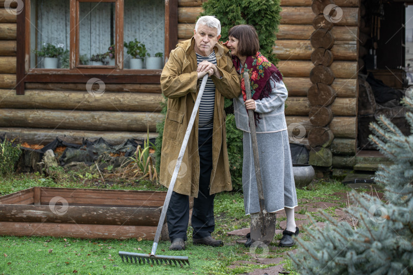 Скачать Деревенская пара пенсионеров позирует возле бревенчатой бани. фотосток Ozero