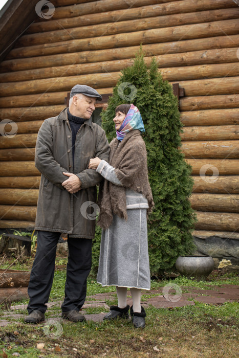 Скачать Деревенская пара пенсионеров позирует возле бревенчатой бани. фотосток Ozero