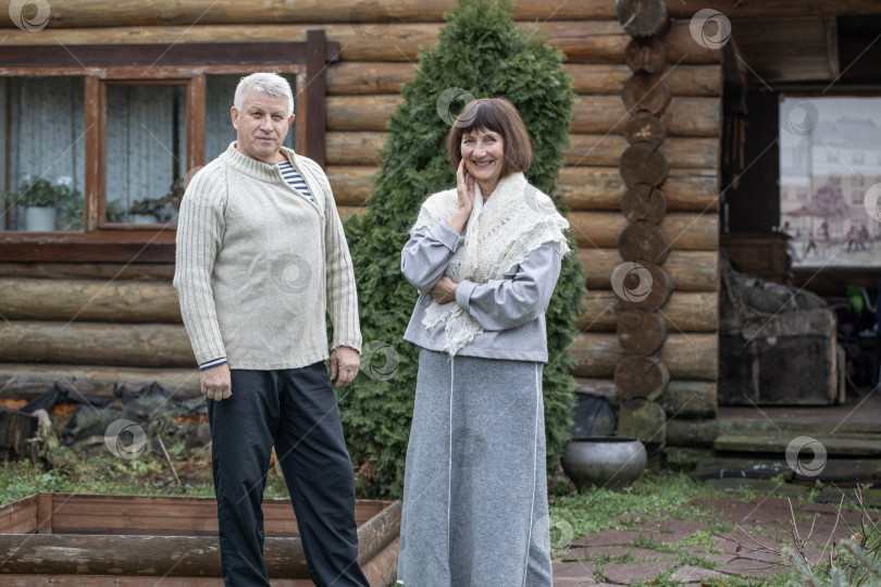 Скачать Деревенская пара пенсионеров позирует возле бревенчатой бани. фотосток Ozero