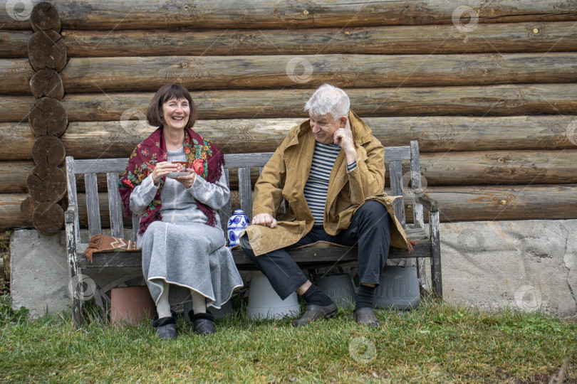 Скачать Деревенские пенсионеры сидят на скамейке возле бревенчатой бани. фотосток Ozero