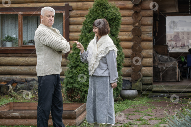 Скачать Деревенская пара пенсионеров позирует возле бревенчатой бани. фотосток Ozero
