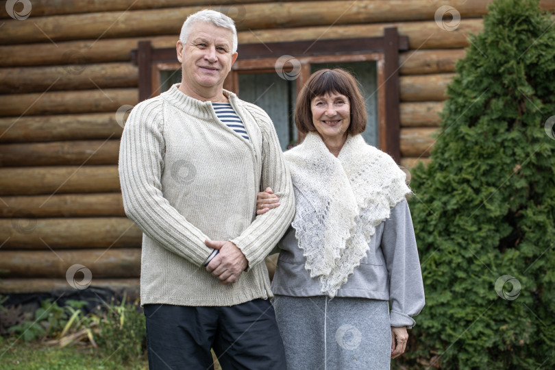Скачать Деревенская пара пенсионеров позирует возле бревенчатой бани. фотосток Ozero