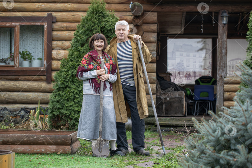 Скачать Деревенская пара пенсионеров позирует возле бревенчатой бани. фотосток Ozero