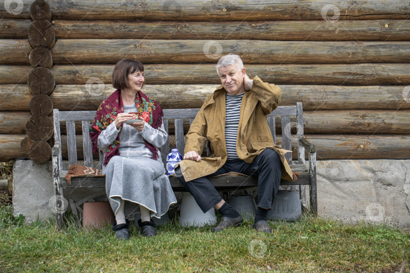 Скачать Деревенские пенсионеры сидят на скамейке возле бревенчатой бани. фотосток Ozero