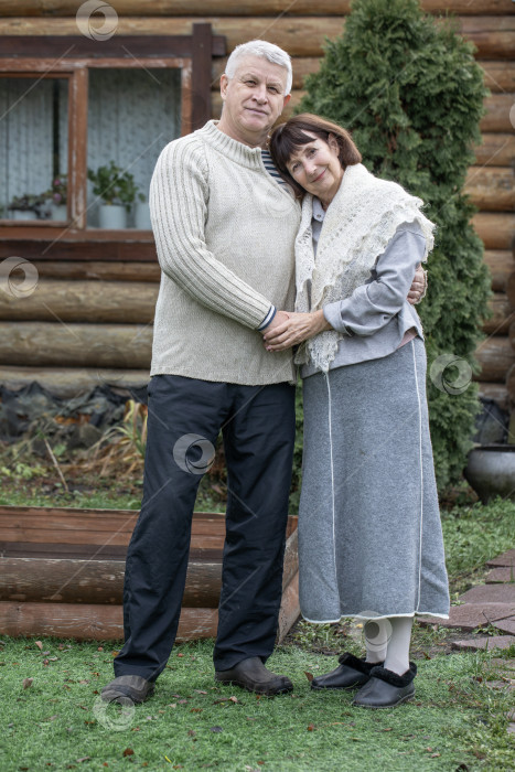 Скачать Деревенская пара пенсионеров позирует возле бревенчатой бани. фотосток Ozero