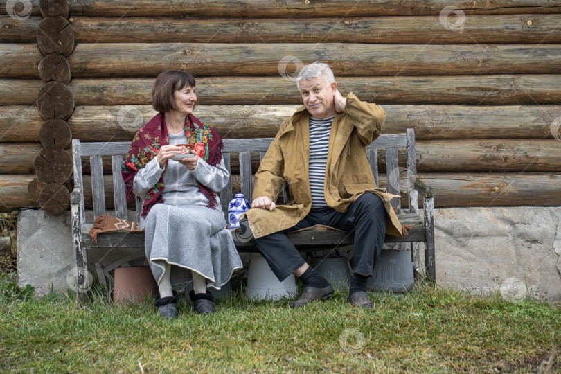 Скачать Деревенские пенсионеры сидят на скамейке возле бревенчатой бани. фотосток Ozero