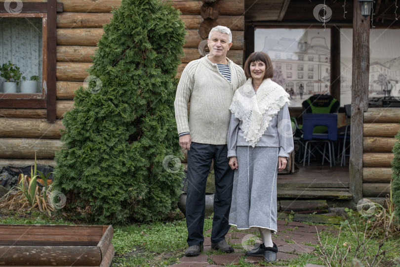 Скачать Деревенская пара пенсионеров позирует возле бревенчатой бани. фотосток Ozero