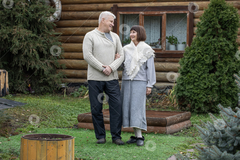 Скачать Деревенская пара пенсионеров позирует возле бревенчатой бани. фотосток Ozero
