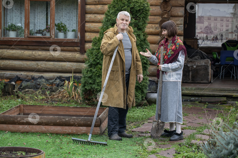 Скачать Деревенская пара пенсионеров позирует возле бревенчатой бани. фотосток Ozero