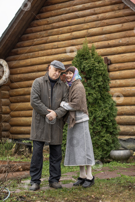 Скачать Деревенская пара пенсионеров позирует возле бревенчатой бани. фотосток Ozero