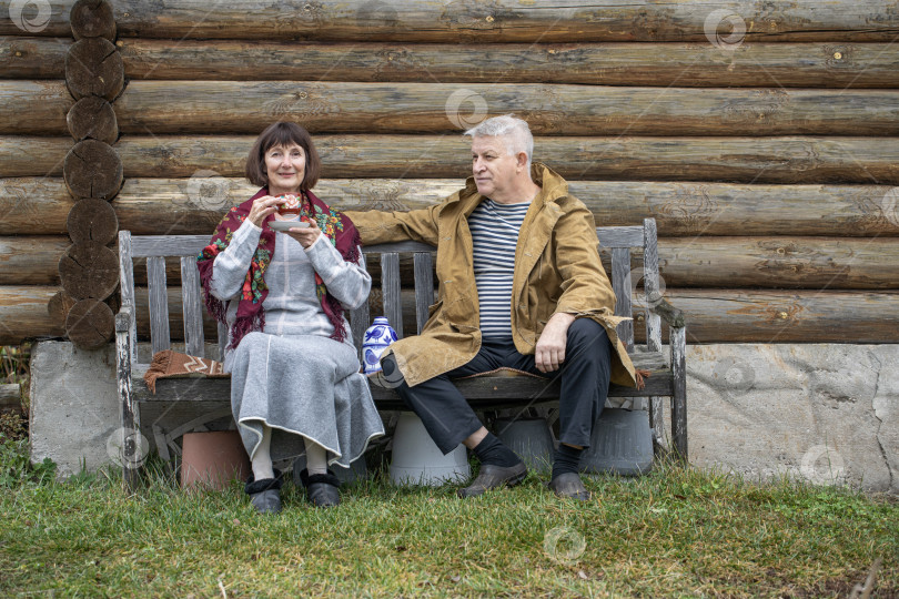 Скачать Деревенские пенсионеры сидят на скамейке возле бревенчатой бани. фотосток Ozero