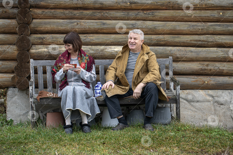 Скачать Деревенские пенсионеры сидят на скамейке возле бревенчатой бани. фотосток Ozero
