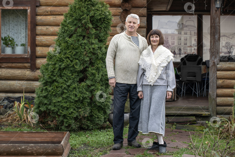 Скачать Деревенская пара пенсионеров позирует возле бревенчатой бани. фотосток Ozero