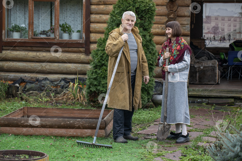 Скачать Деревенская пара пенсионеров позирует возле бревенчатой бани. фотосток Ozero