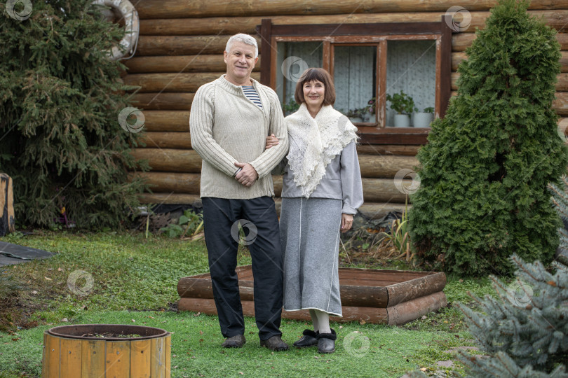 Скачать Деревенская пара пенсионеров позирует возле бревенчатой бани. фотосток Ozero