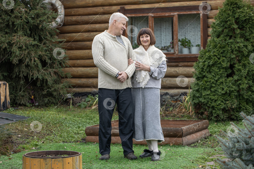 Скачать Деревенская пара пенсионеров позирует возле бревенчатой бани. фотосток Ozero