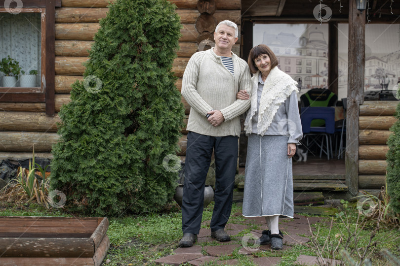 Скачать Деревенская пара пенсионеров позирует возле бревенчатой бани. фотосток Ozero