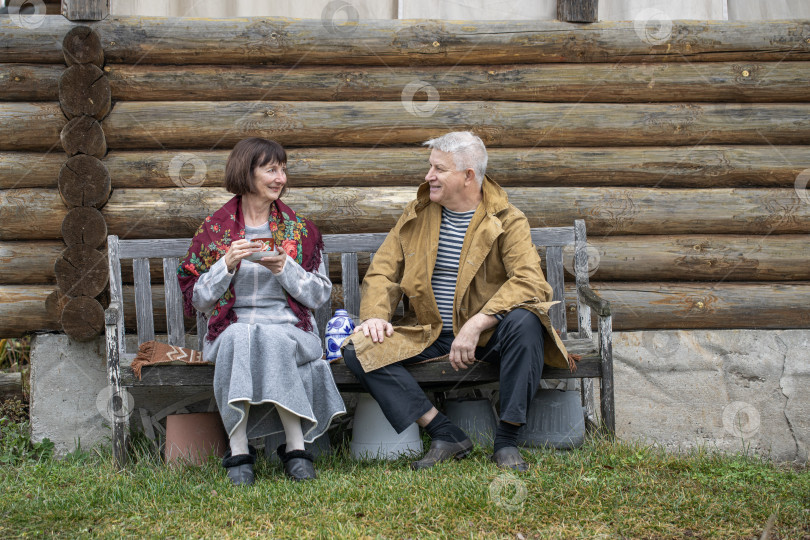 Скачать Деревенские пенсионеры сидят на скамейке возле бревенчатой бани. фотосток Ozero